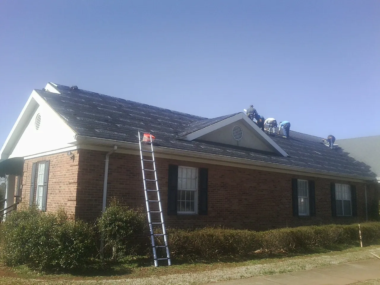 Crew tearing shingles off a brick ranch roof with a ladder set — Metal Roof Repair work by our crew in Easton